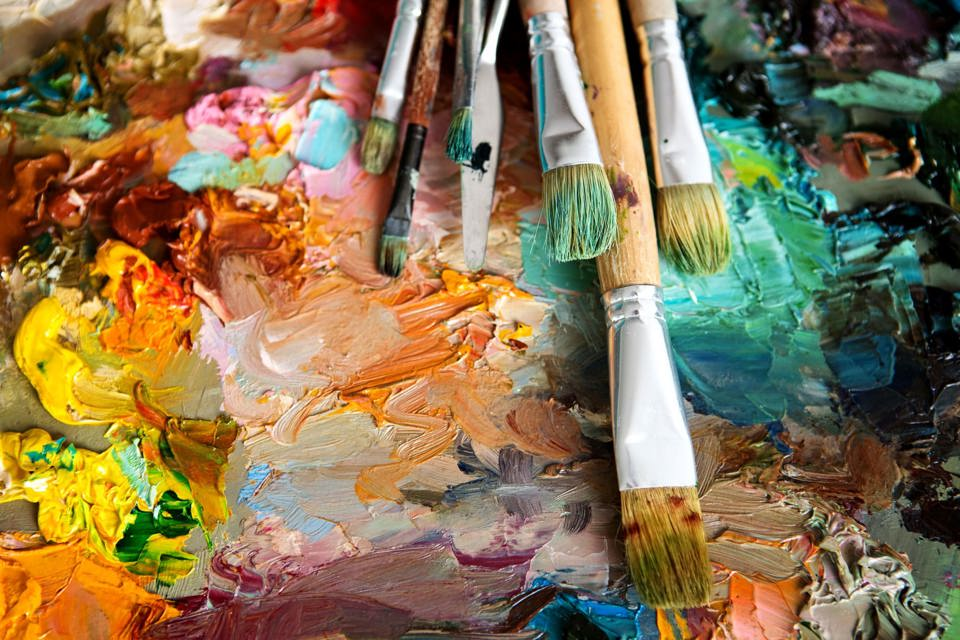 Different sized paint brushes lying on top of an abstract painting