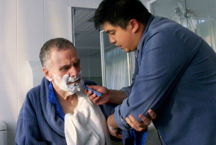 Carer assisting man with shaving