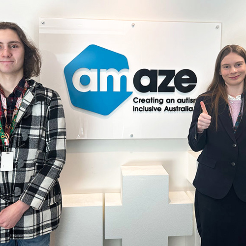 Two individuals pose together in front of a large, illuminated "amaze" sign, smiling and giving a thumbs up.