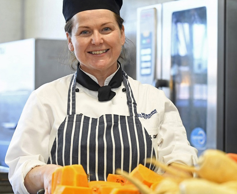 Melbourne polytechnic food staff member smiling at camera while they prepare food.