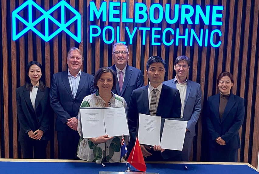 Frances Coppolillo, Chief Executive of Melbourne Polytechnic, holding a signed memorandum of understanding with delegates from Sichuan College of Architectural Technology and various government representatives standing beside her smiling