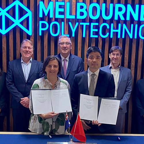 Frances Coppolillo, Chief Executive of Melbourne Polytechnic, holding a signed memorandum of understanding with delegates from Sichuan College of Architectural Technology and various government representatives standing beside her smiling