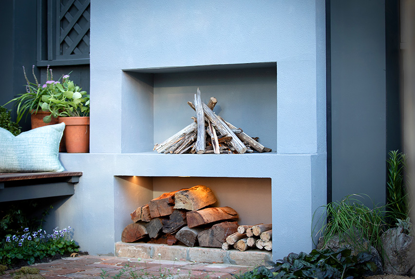 Leigh Hudson's design, 'Ever-Growing Gardens': A cozy outdoor fireplace surrounded by logs and plants.