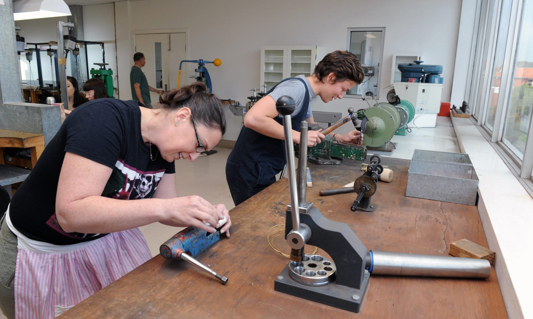 Two jewellery students working with items in vices in the jewellery workshop