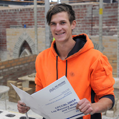 Trade worker smiling at camera while holding Melbourne Polytechnic Bricklaying and Blocklaying manual.
