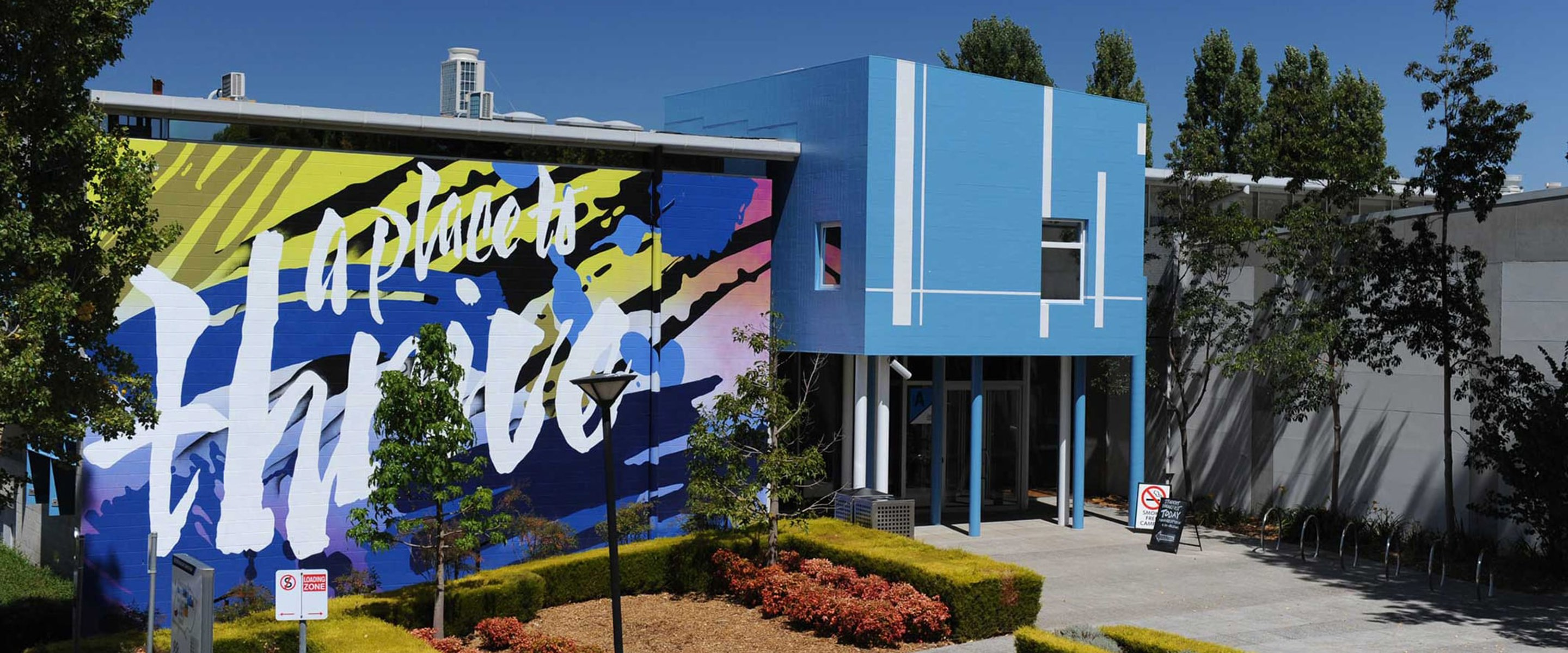 Facade of Greensborough campus. The entry is a blue building with a large mural that says "a place to thrive" on a blue, pink and yellow background