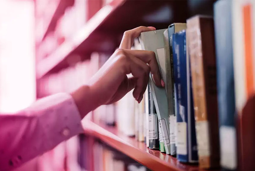 Woman's hands reaching for a book from the library shelf