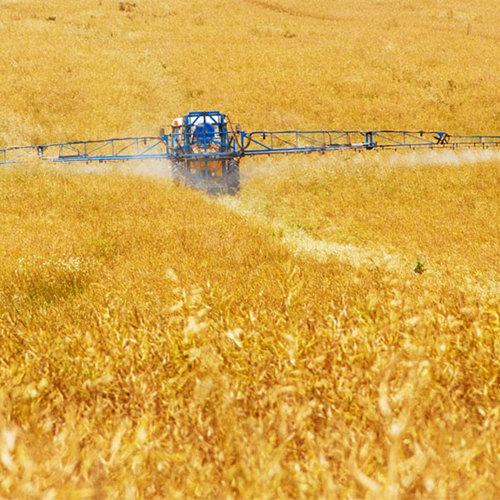 A tractor boom sprayer drives through a crop of wheat