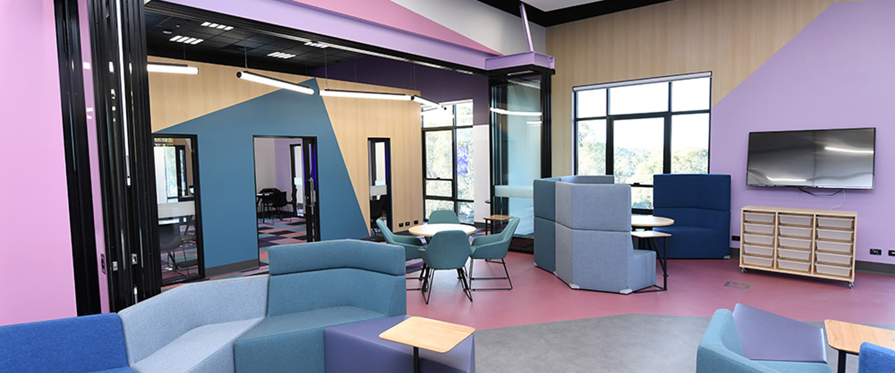 Modern classroom with pink and violet walls and odd geometric shaped furniture.