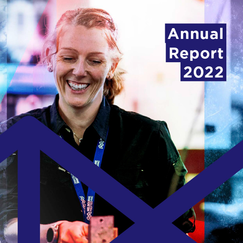 Woman in dark shirt smiling and wearing a Melbourne Polytechnic lanyard whilst working in a workshop, overlaid with a large Melbourne Polytechnic logo and text 'Annual Report 2022'.