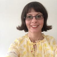 Portrait of Dr. Nicola Cooley. Smiling woman with brown hair, glasses, and a yellow floral blouse.