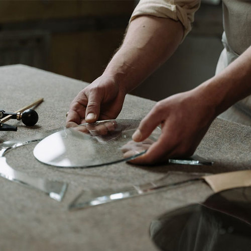 Artist's hand measuring and cutting a glass circle with tools around them