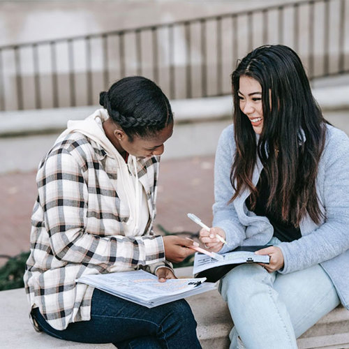 Two female students smiling while studying outside