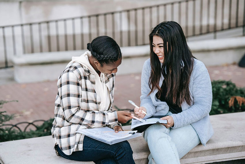 Two female students smiling while studying outside
