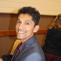 Portrait of Prasanna Gunasinghe smiling at camera and wearing a grey suit with dark red shirt with black stripes.