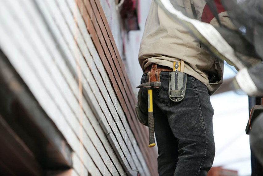 The back of a carpenter showing his tool belt with a hammer and measuring tape 