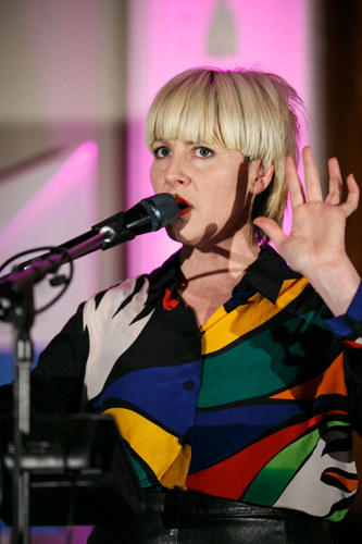 Louise Terry wearing a colourful shirt and singing into a microphone.