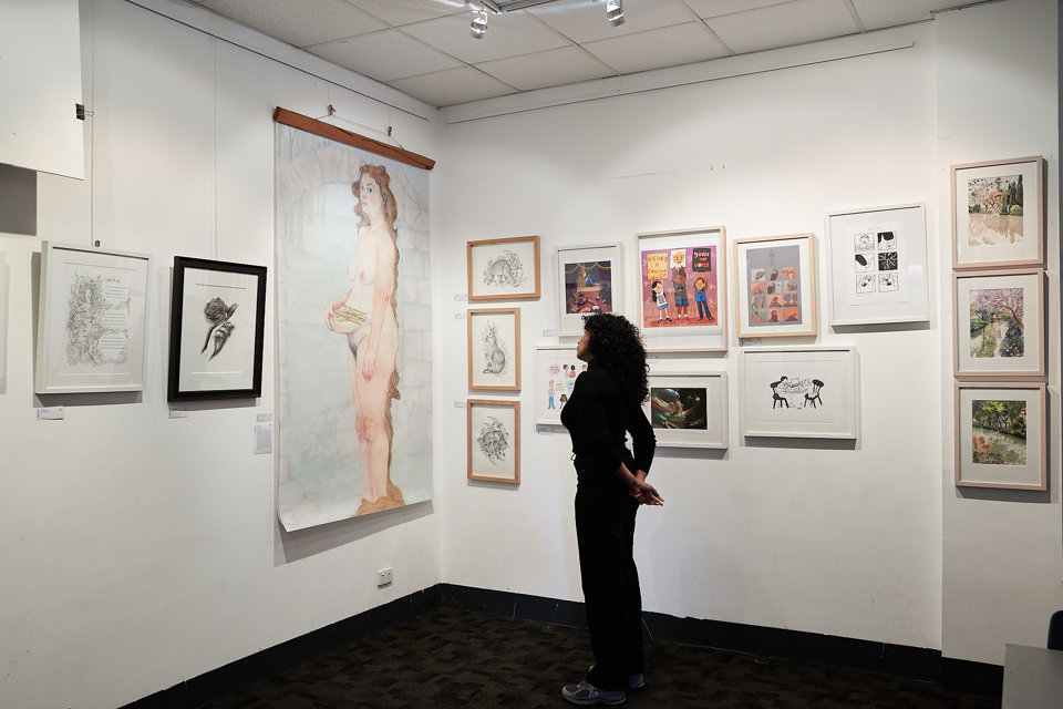 A gallery wall with student illustration artwork displayed. A visitor is viewing an illustration.