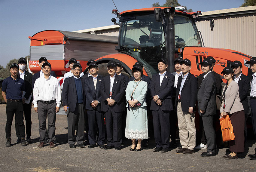 A group of people wearing Kubota caps gathered in front of an orange Kubota tractor.