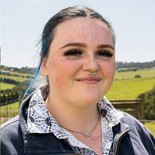 Woman with blue hair and shirt standing in front of field smiling