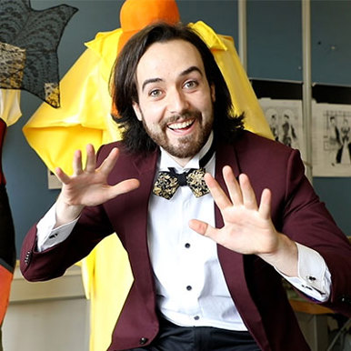 A male theatre student dressed in a suit and bow tie ecstatically smiles at the camera. 