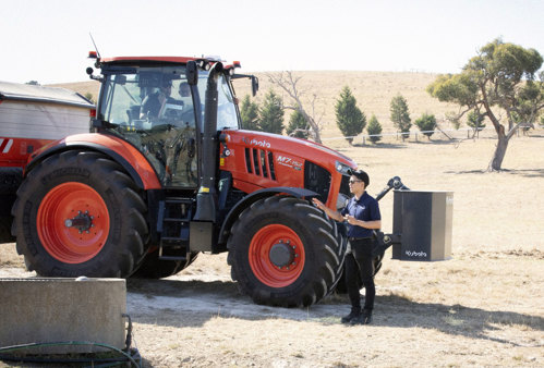 A man standing confidently beside a red and black tractor on a property talking to someone off screen