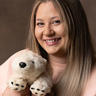 A girl with blonde hair smiles at the camera while holding her white polar bear toy 