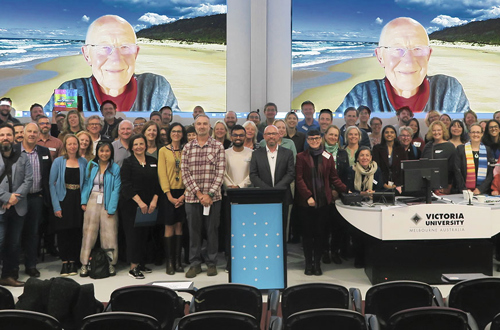 A diverse group of people standing in front of a large screen at a conference