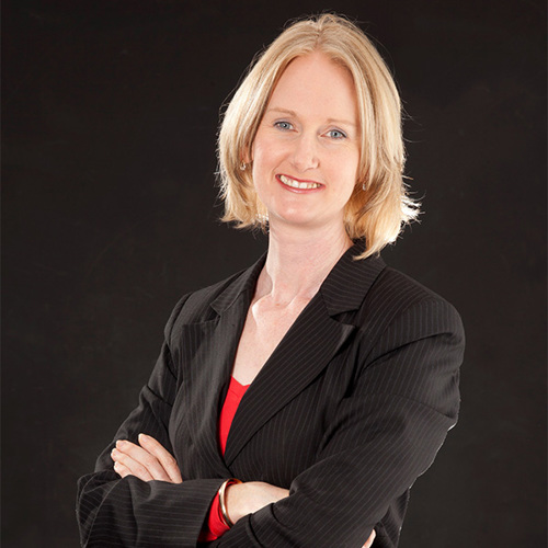 Portrait of Rachael Cowley smiling with crossed arms and wearing a suit jacket.