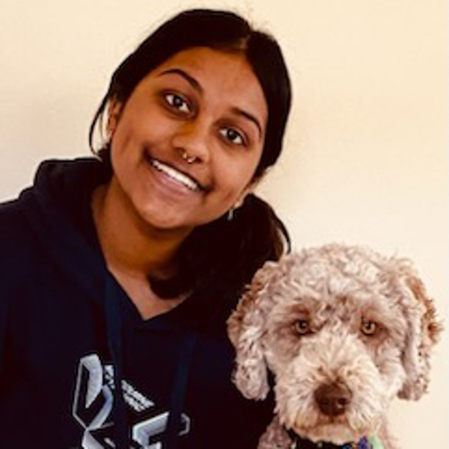 Ishaana Tharan wearing a hoodie and smiling while sitting beside a grey dog.