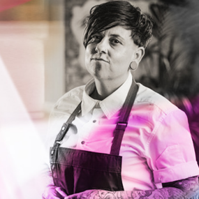 Image of Telina Menzies, a chef, with a confident stance, dressed in a chef's apron over a white shirt, set against a monochrome background with a splash of pink overlay.