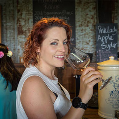 A woman with red hair smiling while holding a glass of wine at a social event.