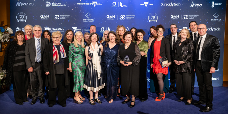 A group of professionals posing together on a blue carpet, representing award winning collaboration in an engaging environment.